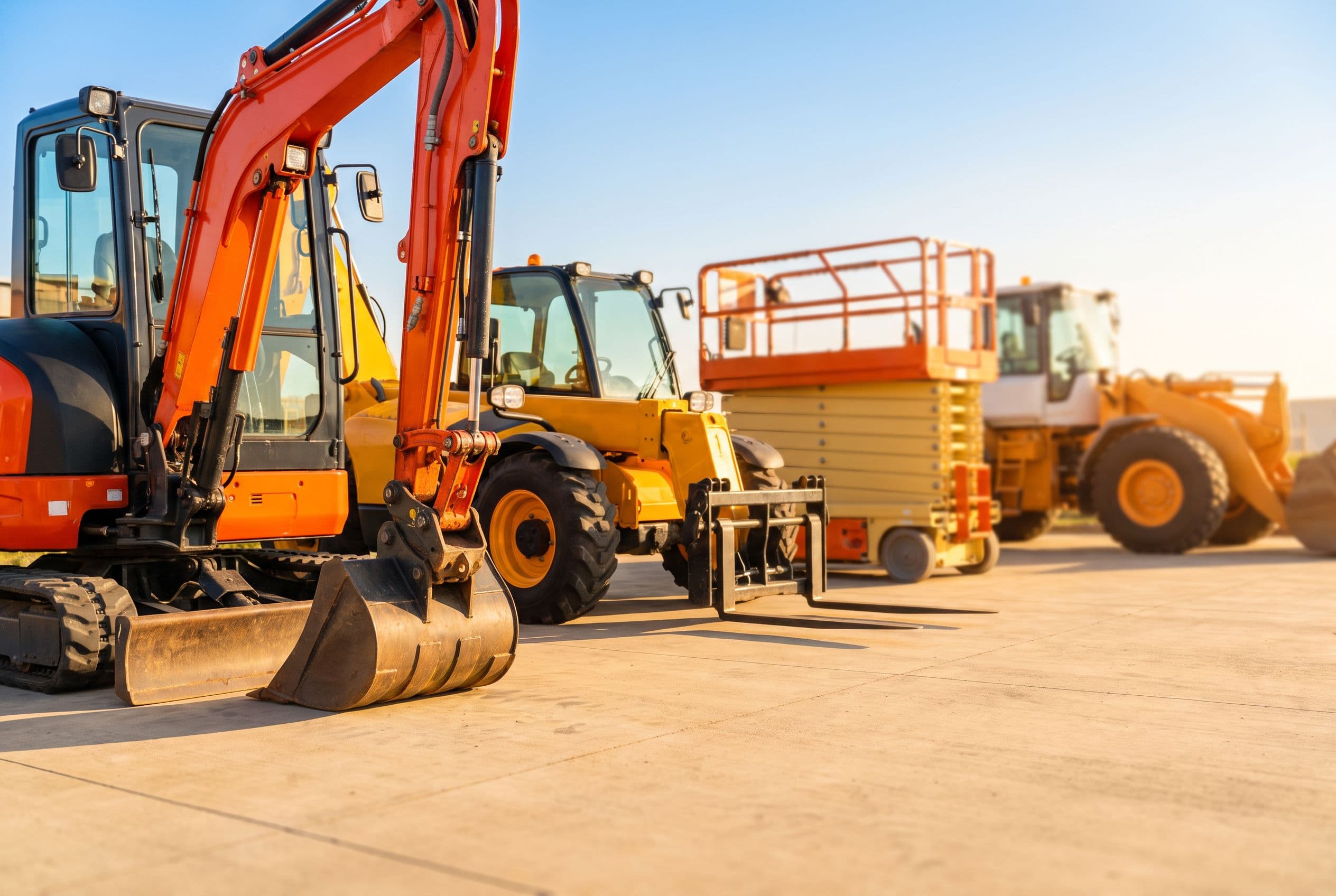 A row of rental machines lined up on clean concrete in a bright equipment yard.